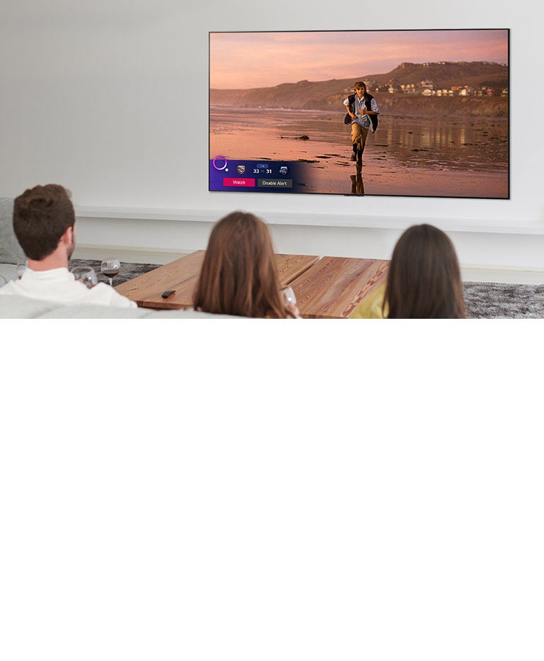 Three people watching TV screen showing a scene from a fantasy movie with a Sports Alert