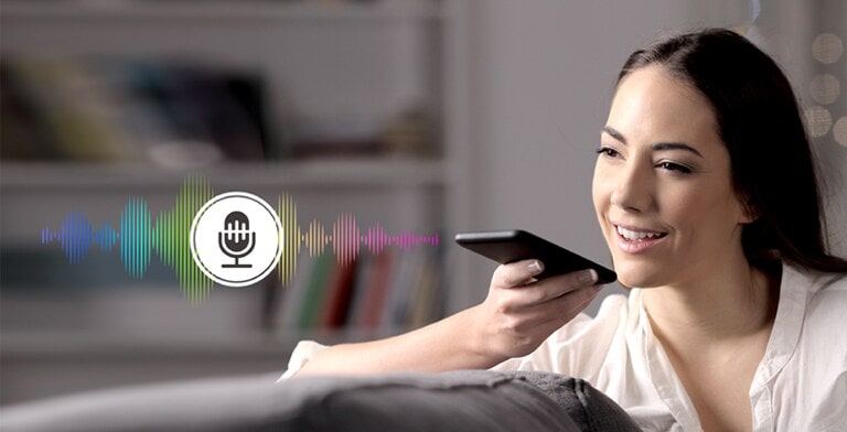 A woman is controlling TV by speaking to a remote control which has voice recognition.