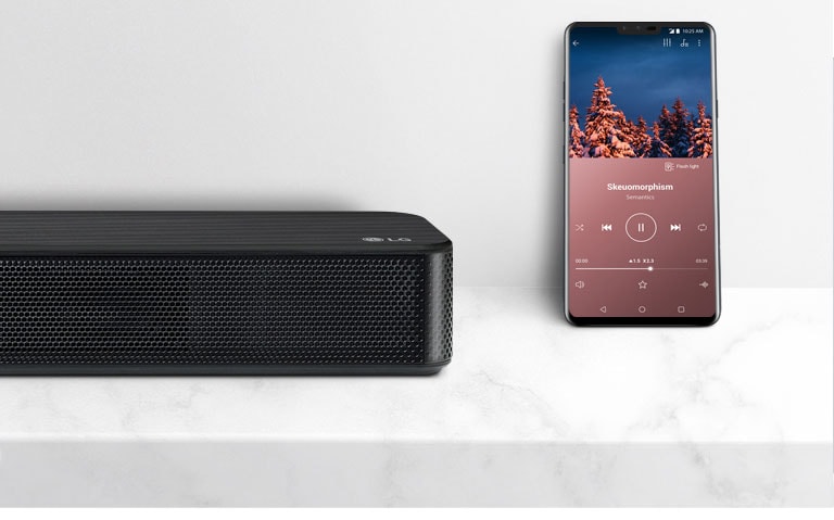 LG horizontaliojo garsiakalbio šalia išmaniojo telefono dešinės pusės vaizdas stambiu planu Du įrenginiai padėti ant baltos lentynos.