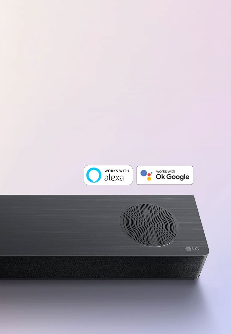 LG horizontalusis garsiakalbis „Sound Bar“ padėtas ant žemės, ant horizontaliojo garsiakalbio dešiniojo kampo pavaizduotas LG logotipas. Ant horizontaliojo garsiakalbio uždėtas „Alexa“ logotipas ir OK GOOGLE  logotipas.