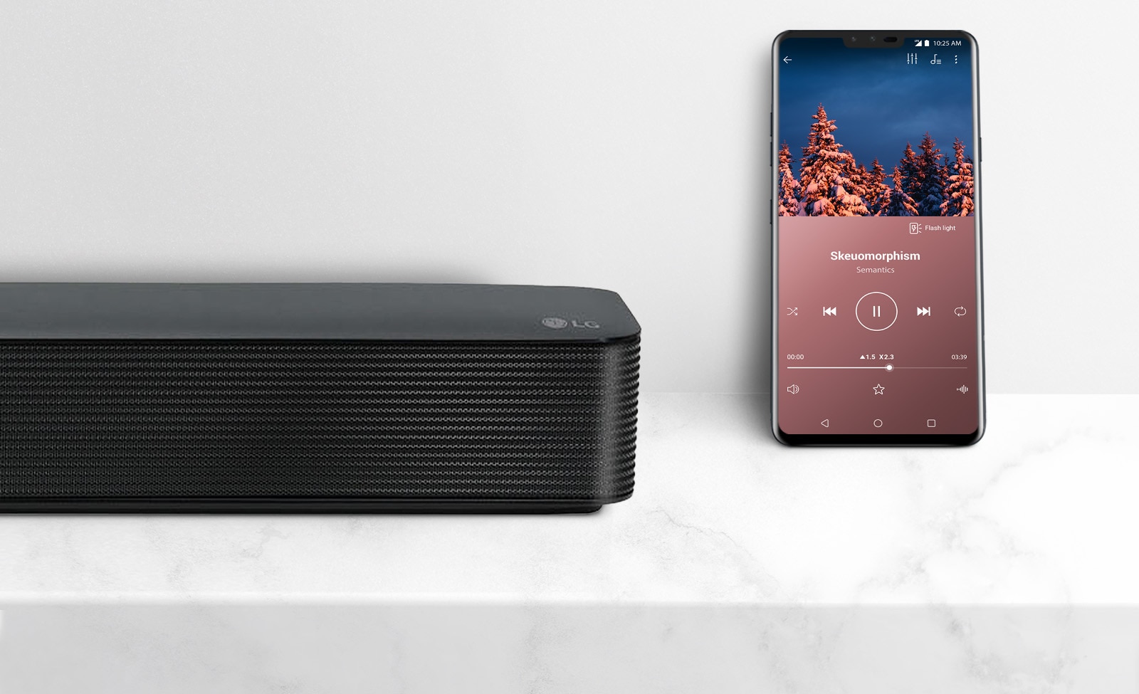 Priartinta LG Soundbar dešinioji pusė šalia išmaniojo telefono. Du įrenginiai ant baltos lentynos.