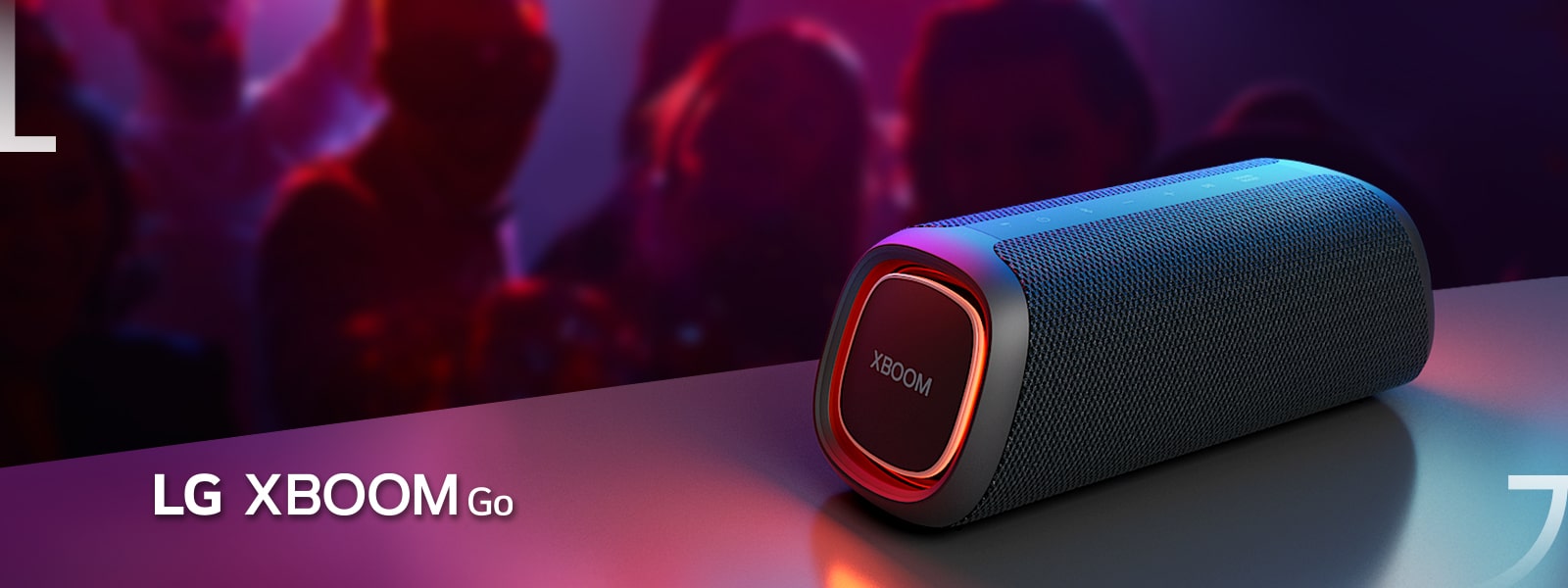 LG XBOOM Go XG5 padėtas ant metalinio stalo su įjungtu oranžiniu apšvietimu. Už stalo žmonės mėgaujasi muzika.
