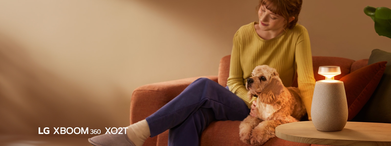 Moteris sėdi ant sofos su šunimi ir klausosi muzikos su LG XBOOM 360 XO2T.