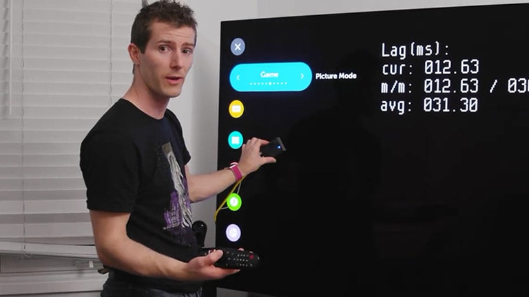 Nuomonės žaidimų srityje formuotojas kanalo „Linus Tech Tips“ vedėjas rodo pateiktį apie LG OLED mažą įvesties delsą priešais LG OLED TV ekraną