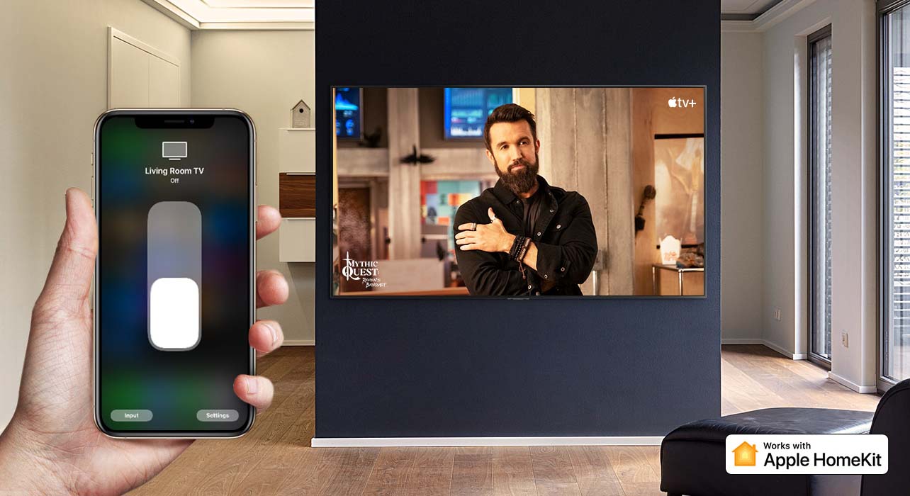 Televizorių „iPhone“ įrenginiu valdanti ranka stambiu planu ir televizorius, kuriame rodomas „Apple TV+“ turinys