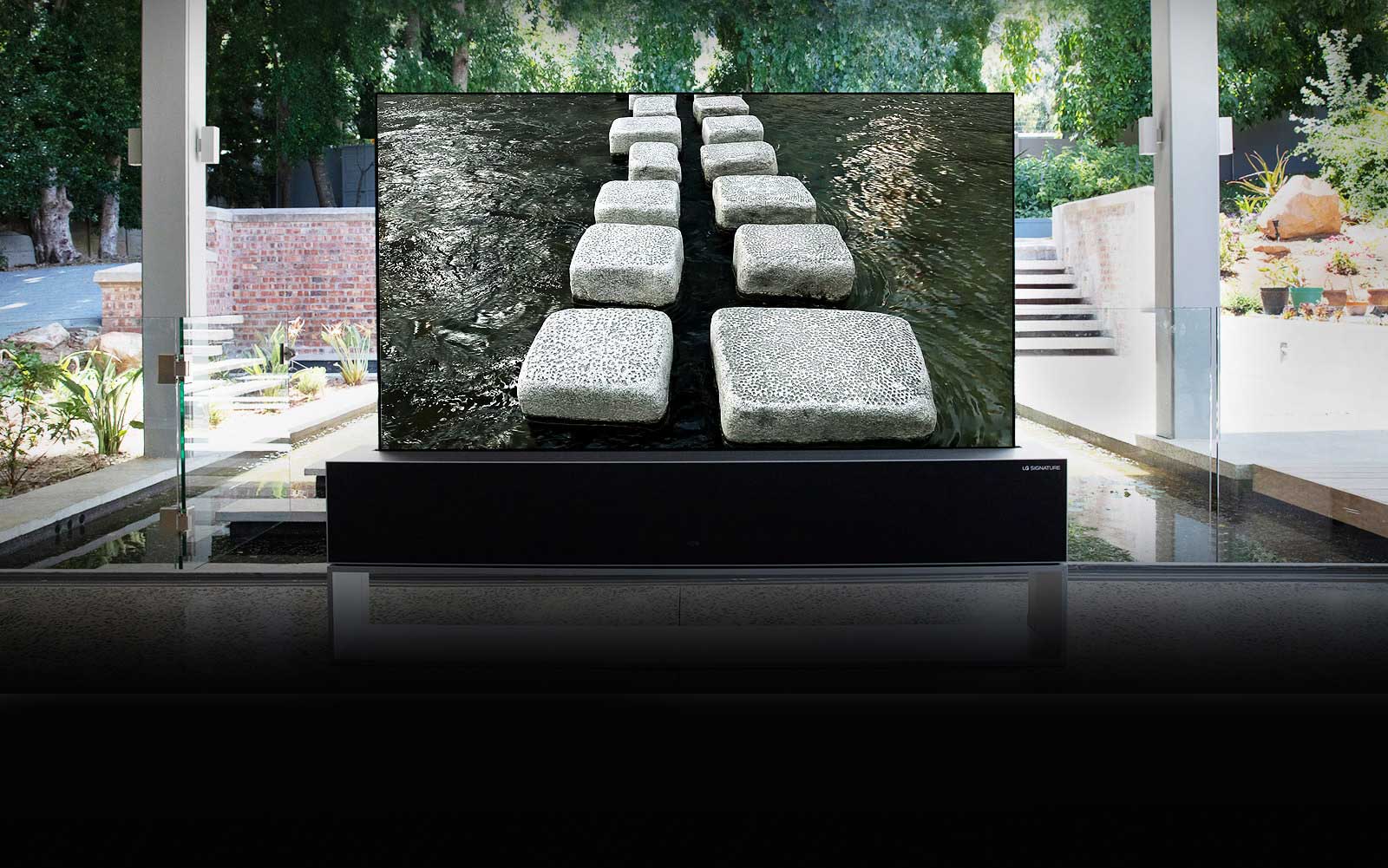 Priešais prabangius namus su tvenkiniu esančiame suvyniojamame televizoriuje rodomas tiltas iš akmeninių blokelių (slinkite puslapiu žemyn)