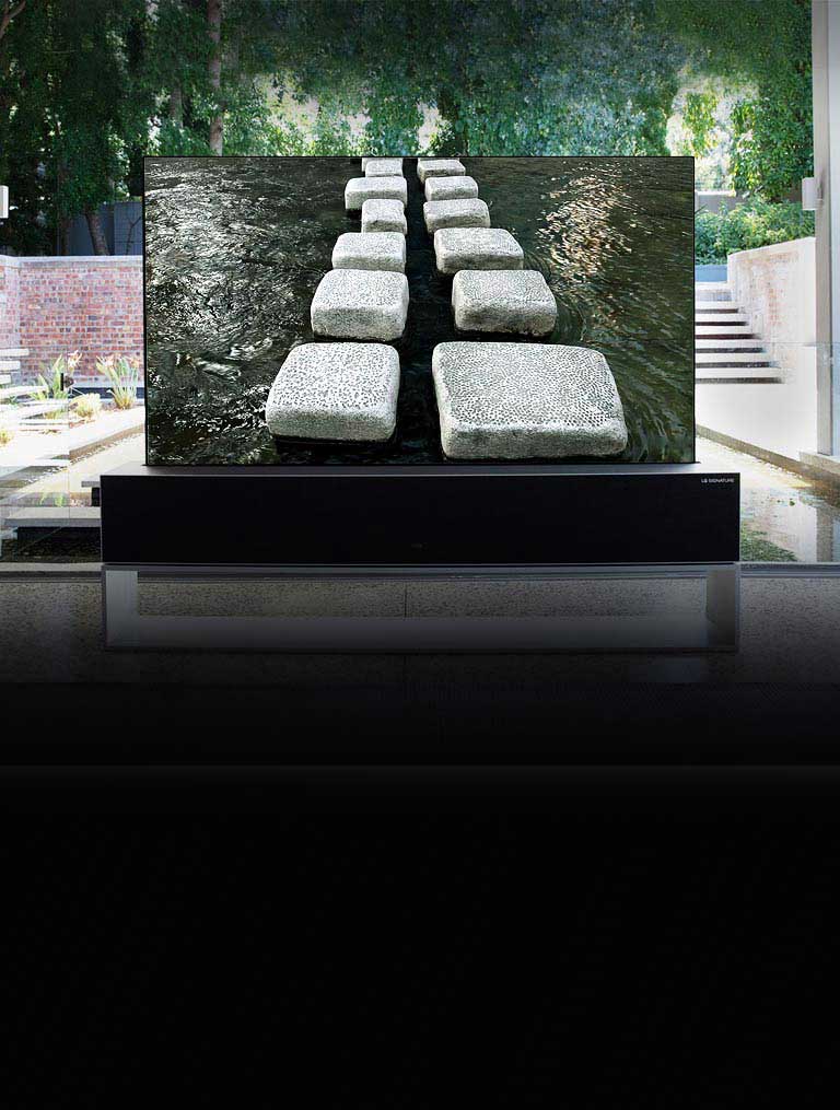 Priešais prabangius namus su tvenkiniu esančiame suvyniojamame televizoriuje rodomas tiltas iš akmeninių blokelių (slinkite puslapiu žemyn)