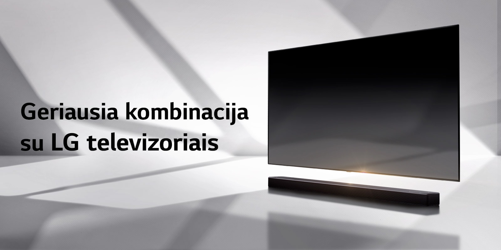 Horizontalusis garsiakalbis ir televizorius pastatyti ant baltų grindų, o už jų krenta šešėlis iš lauko.