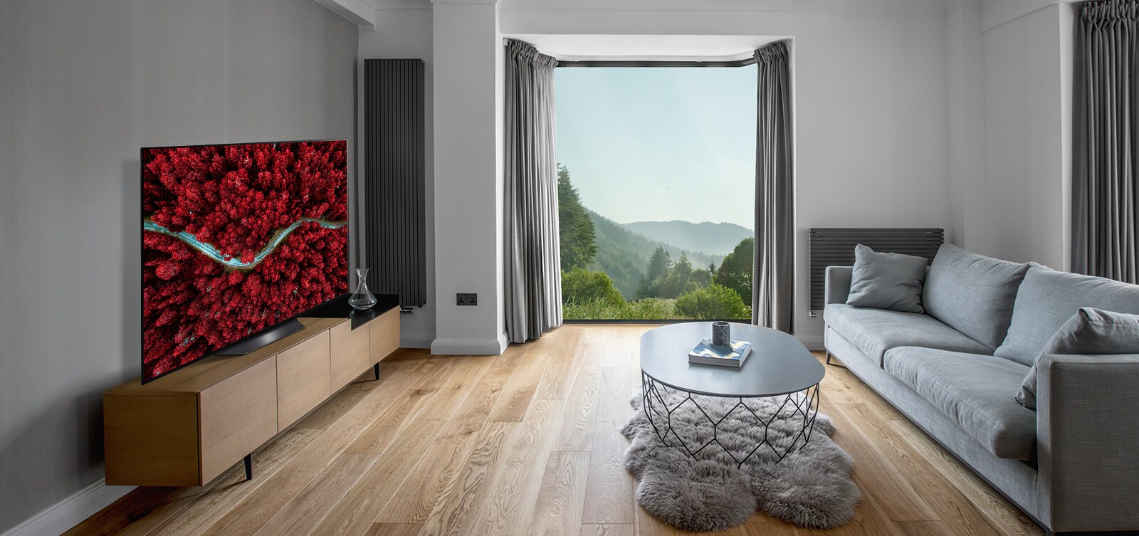 Svetainė su sofa ir televizorius, kuriame vaizduojamas iš aukštai nufilmuotas peizažas