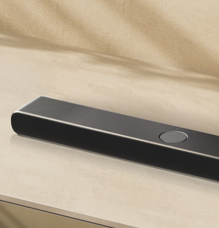 LG „Soundbar“ smėlio spalvos fone iš viršaus ir kampu. 