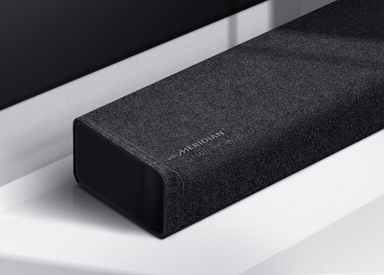 LG horizontaliojo garsiakalbio su „Meridian“ logotipu apatiniame kairiajame kampe kairės pusės vaizdas stambiu planu. Taip pat matoma televizoriaus apatinė kairioji pusė.