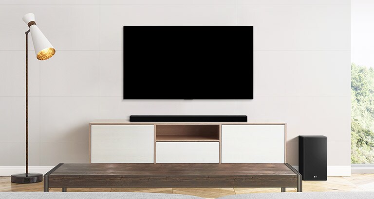 Televizorius, Soundbars ir žemadažnis garsiakalbis, pastatyti kuklioje svetainėje.