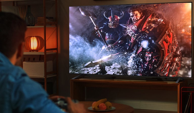 Ant sofos tamsiame kambaryje sėdi vyras ir dideliame TV žaidžia RPG žaidimą.
