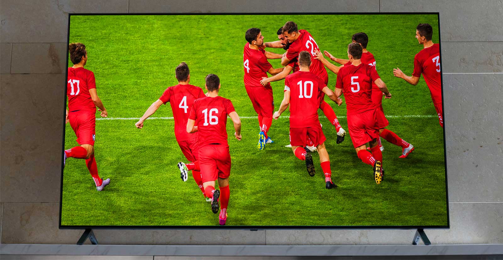 „Nanocell TV“ ant TV stovo. Futbolo žaidėjai džiaugiasi.