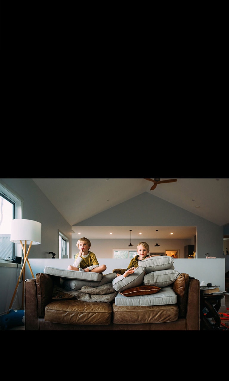 Ant sofos sėdintys dvyniai kažką žiūri per televizorių.