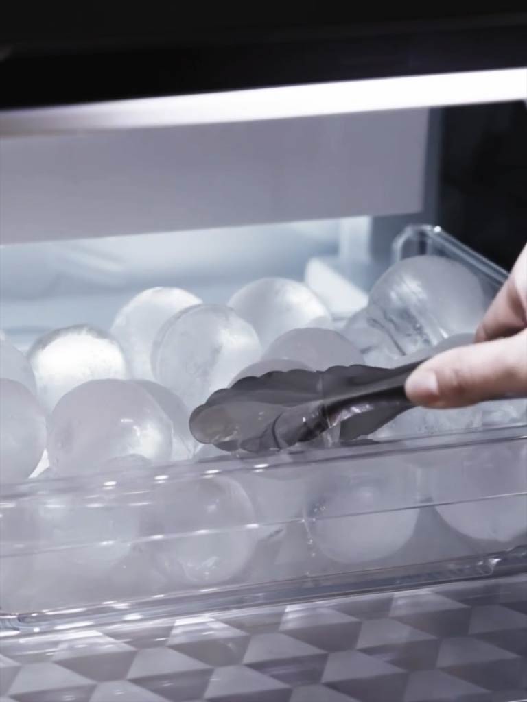 Žnyplės, imančios apvalų ledo rutuliuką nuo šaldiklyje esančio skaidraus padėklo