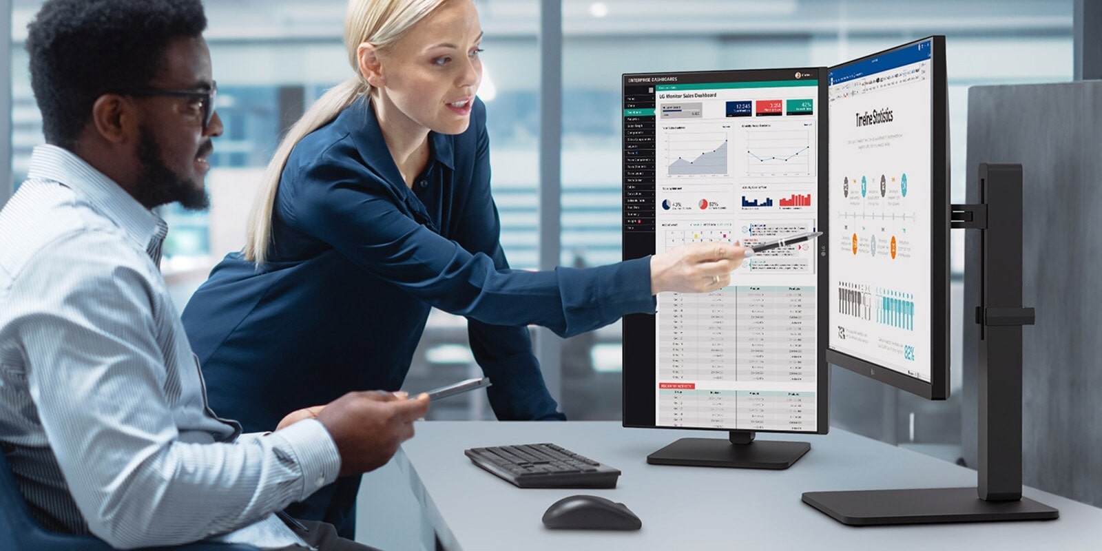 Du darbuotojai vyras ir moteris diskutuoja žiūrėdami į monitorių biure.