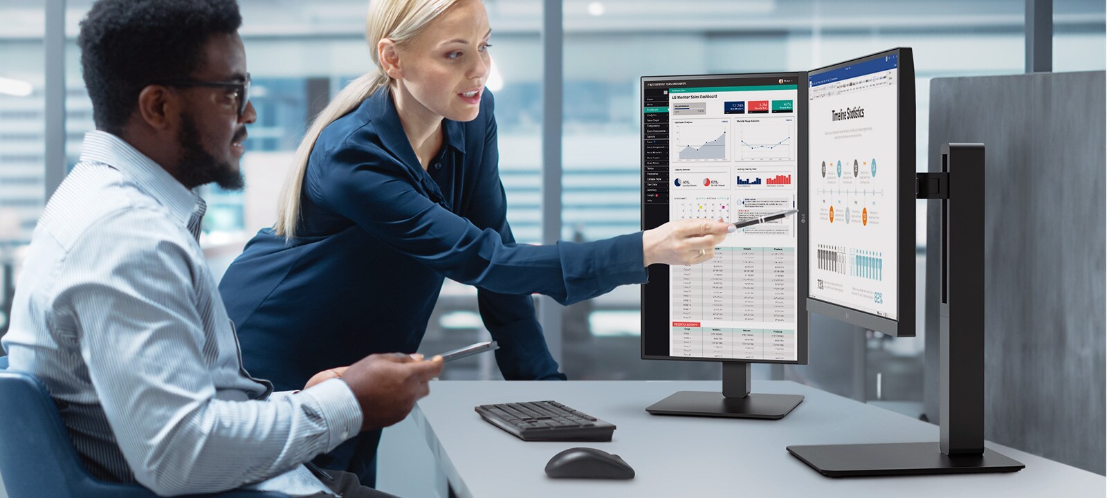 Du darbuotojai vyras ir moteris diskutuoja žiūrėdami į monitorių biure.