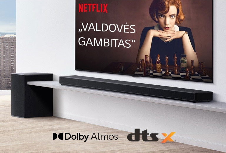 Ant sienos įrengtas televizorius. Televizoriaus ekrane rodomas TV laidos plakatas. „LG Soundbar“ yra tiesiai po televizoriumi ant baltos lentynos, o šalia yra žemadažnis garsiakalbis. Paveikslėlio apatinėje vidurinėje dalyje yra „Dolby Atmos“ ir DTS:X logotipai.