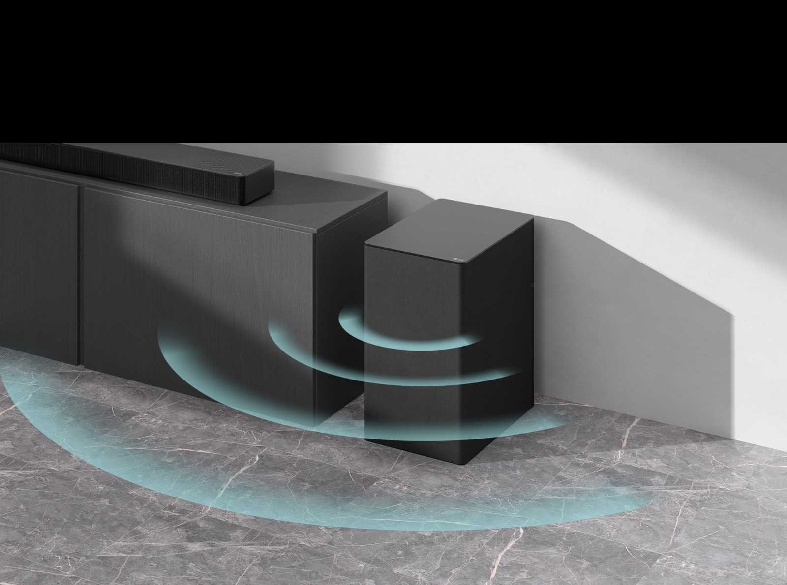 Ant spintelės pastatytas horizontalusis garsiakalbis („sound bar“). Šalia belaidis žemųjų dažnių garsiakalbis, padėtas ant grindų. Iš žemųjų dažnių garsiakalbio sklinda mėlyni garsą vaizduojantys grafiniai vaizdai.