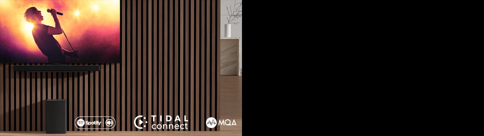 Ant sienos LG OLED C, o žemiau – „LG Sound Bar SC9S“, įrengtas ant išskirtinio laikiklio. Po juo – žemųjų dažnių garsiakalbis. Televizoriuje rodoma koncerto scena.
