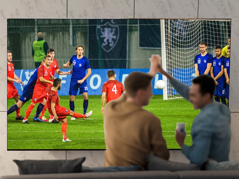 Žmonės svetainėje itin dideliame TV ekrane stebi sporto rungtynes