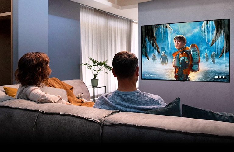 Svetainėje pora sėdi ant sofos ir per TV žiūri romantinį filmą