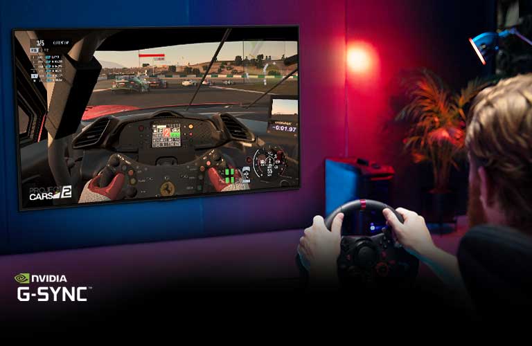 Vyras sėdi lenktynių žaidimų kėdėje, laiko lenktyninio automobilio vairą ir žaidžia lenktynių žaidimą TV ekrane