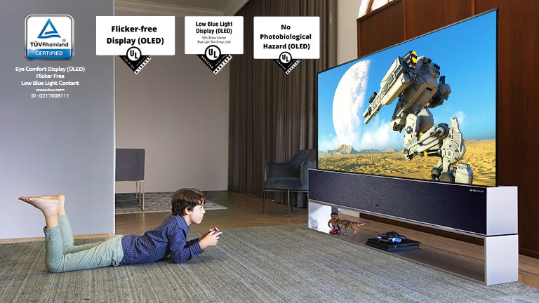 Ant grindų gulintis vaikas, laikantis žaidimų pultą ir žaidžiantis žaidimą TV ekrane