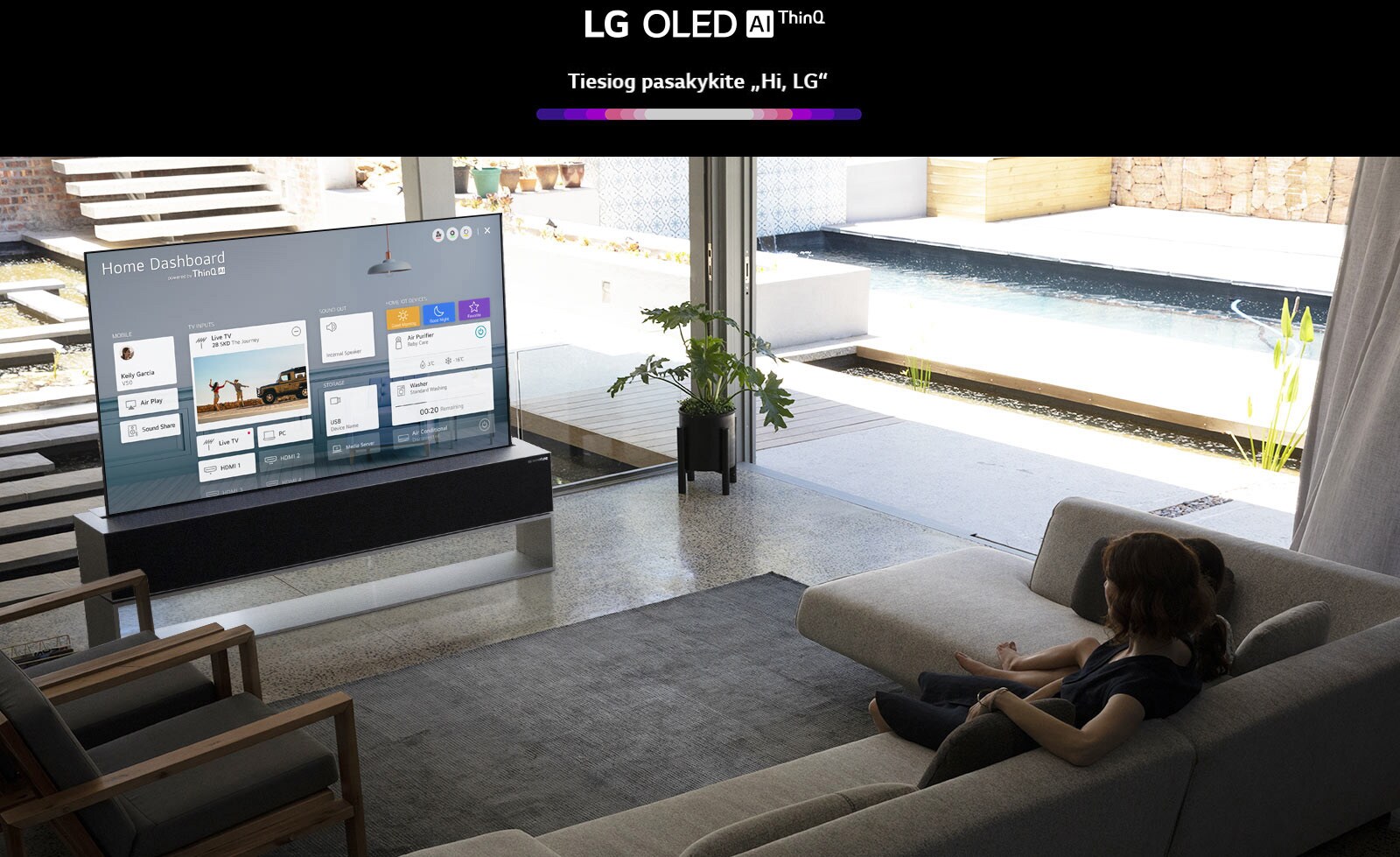 Svetainėje ant kėdės sėdinti moteris, TV ekrane rodomas namų skydelis