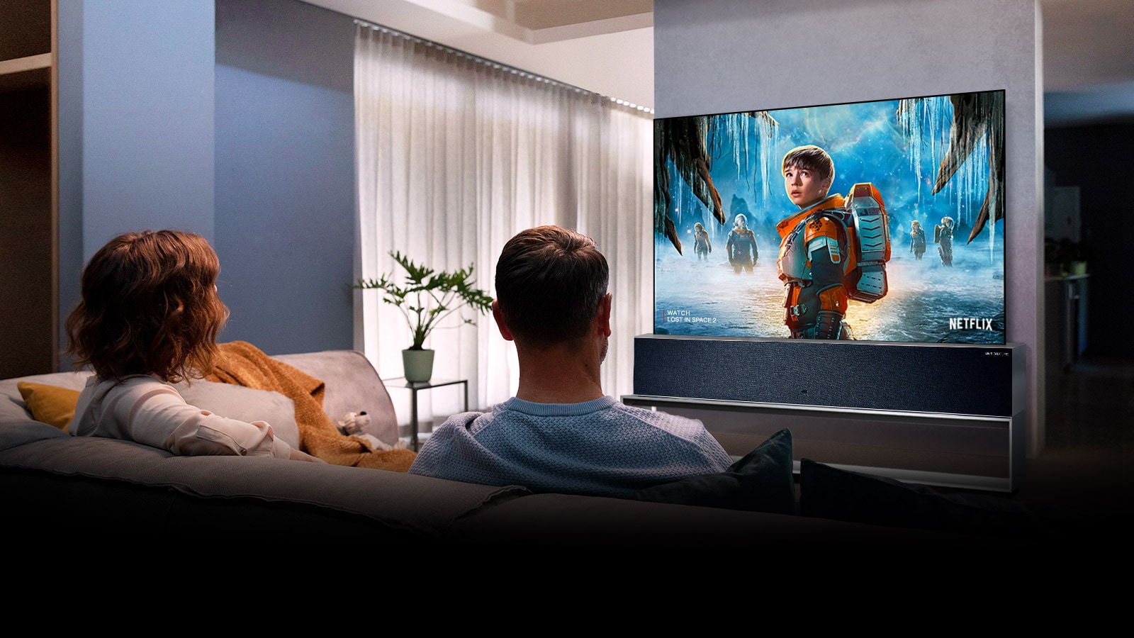 Svetainėje pora sėdi ant sofos ir per TV žiūri filmą PASIKLYDĘ ERDVĖJE 2