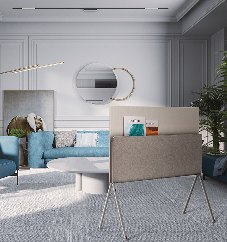 Mėlynų atspalvių svetainėje, pro kurios langą matoma pakrantė, iš galinės pusės vaizduojamas LG OLED Posé, o ant knygų lentynėlės padėti žurnalai.
