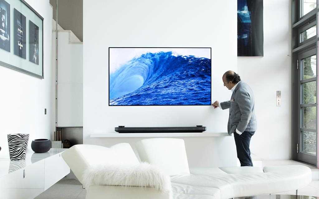 LG W7 OLED TV in an all-white minimalist living room with a man looking at it closely