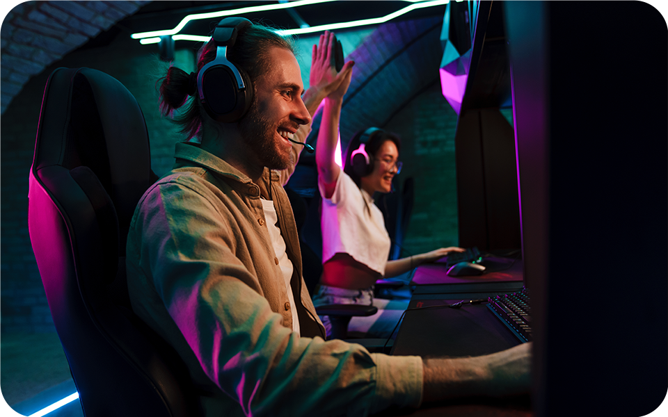 Du žaidėjai intensyviai sutelkė dėmesį į 4K monitorių silpnai apšviestoje patalpoje ir mėgavosi įtraukiančia vaizdo žaidimų patirtimi.