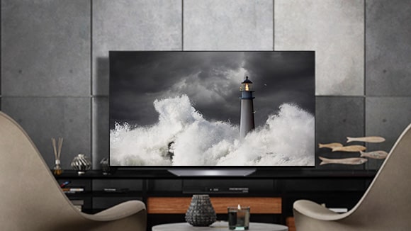 LG OLED B2 pilkame kambaryje su akmeninėmis sienomis, aksesuarais ir į jį nukreiptomis kėdėmis