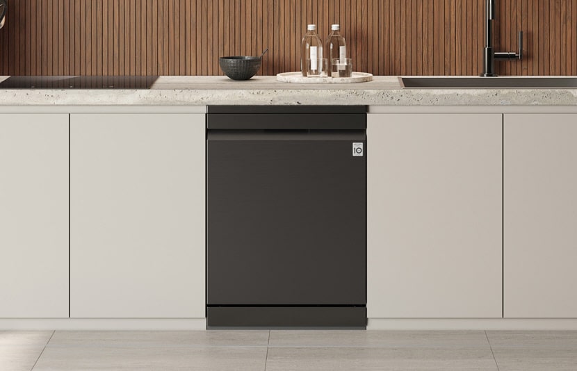 LG iebūvētā trauku mazgājamā mašīna ar elegantu iebūvētu paneļa dizainu uzstādīta vienā līmenī starp baltiem apakšējiem skapīšiem zem akmens virsmas, tā centrēta zem koka sienas apdares ar izlietni, pudelēm un bļodai atrodoties uz letes.