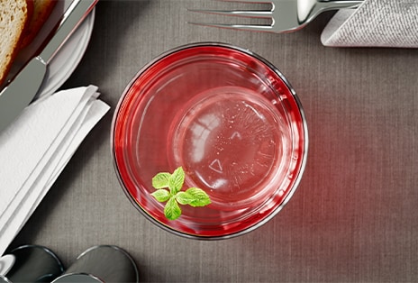 Glāze ar LG Craft Ice™ un piparmētras zariņu uz tumša koka galda, blakus galda piederumiem, salvetēm un ēdiena šķīvim.