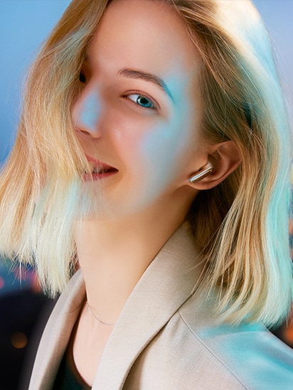 Sieviete ar zelta TONE Free austiņām brīvā dabā skatās uz kameru un priecīgi smaida