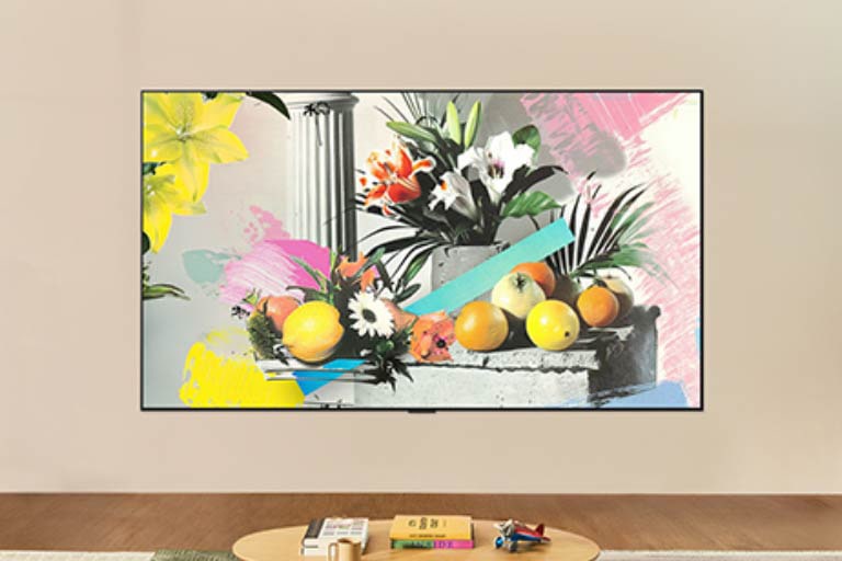 LG QNED evo AI QNED80 Mini LED ir uzstādīts pie sienas gaišā telpā, Galerijas režīmā rādot krāsainu ziedu un augļu mākslas darbu, kamēr spilgtuma kontrole pielāgojas optimālai skatīšanās pieredzei jebkurā apgaismojumā. 