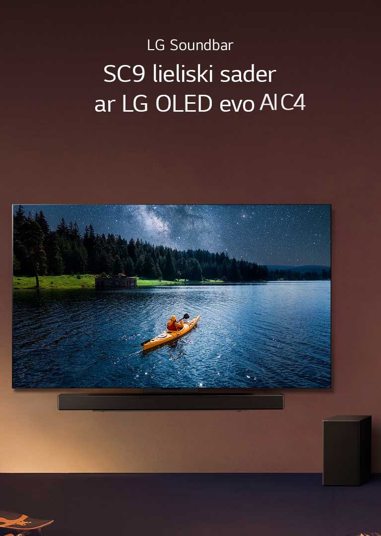 LG TV un Soundbar uzstādīts pie sienas un zemfrekvences skaļrunis uz grīdas pa labi. TV ir redzams cilvēks kajakā uz ezera, un maigas ēnas plūst pāri sienai.