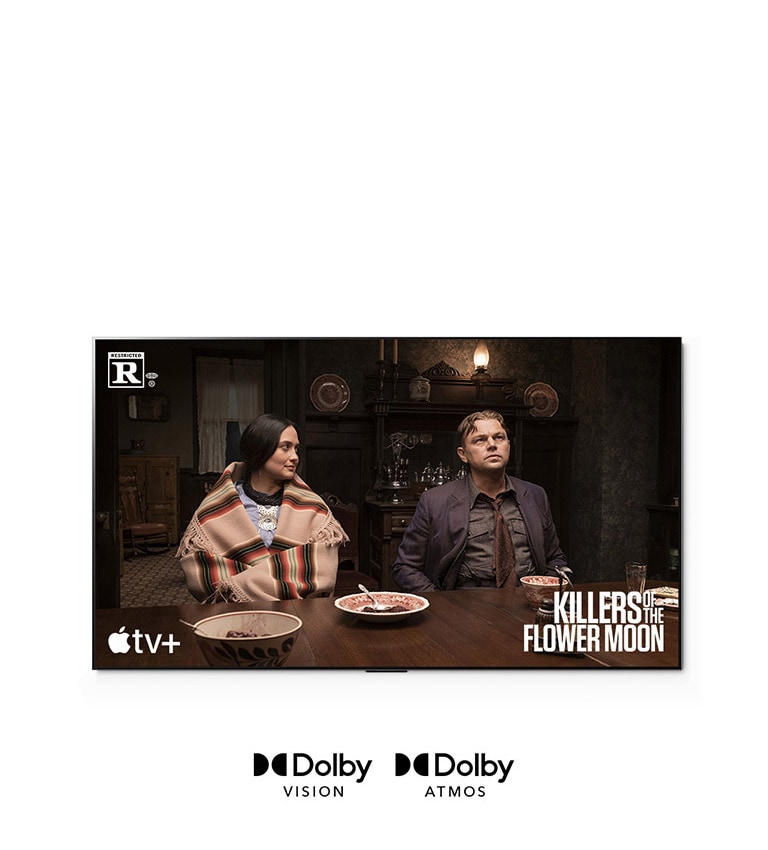 Attēls, kurā vīrietis un sieviete sēž kopā pie galda, kas ir kadrs no filmas “Ziedu mēness slepkavas” (Killers of the Flower Moon).