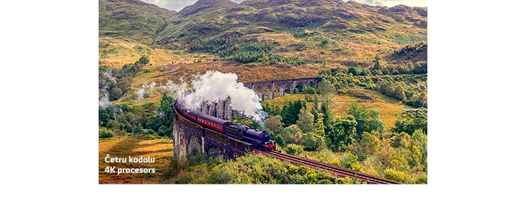 Vilciens brauc pa sliedēm starp kalniem, un no tā gāžas tvaika mutuļi, un apakšējā kreisajā pusē redzams teksts “Četrkodolu 4K procesors”.