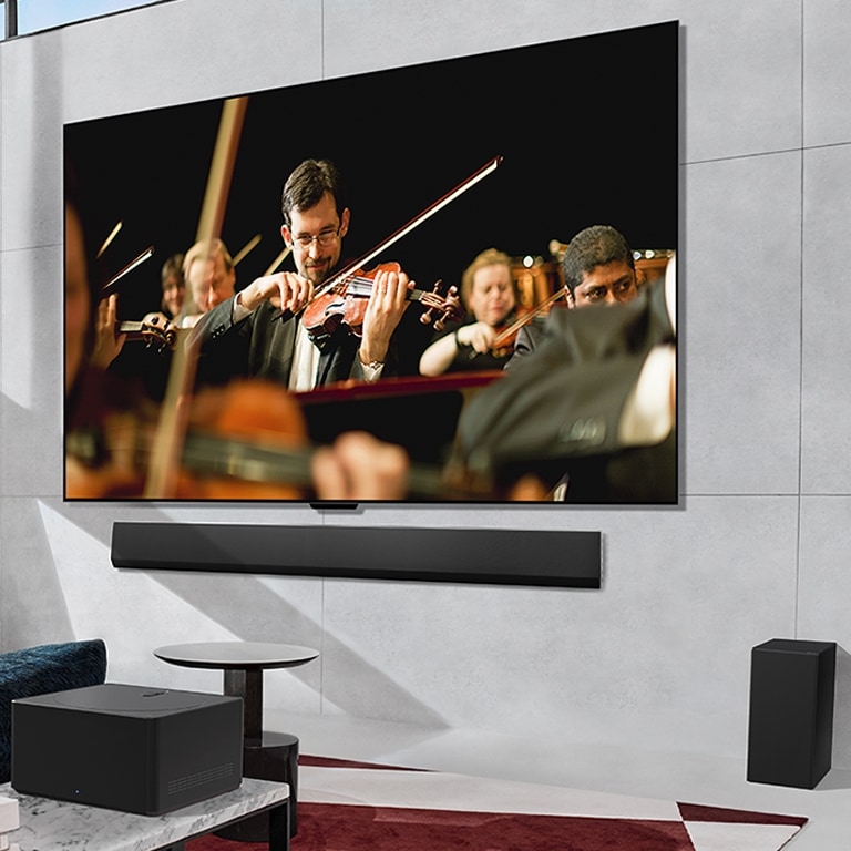 LG OLED TV, kas spēlē orķestri uz ekrāna, kas piestiprināts pie sienas, un Zero Connect Box, kas novietots priekšā.