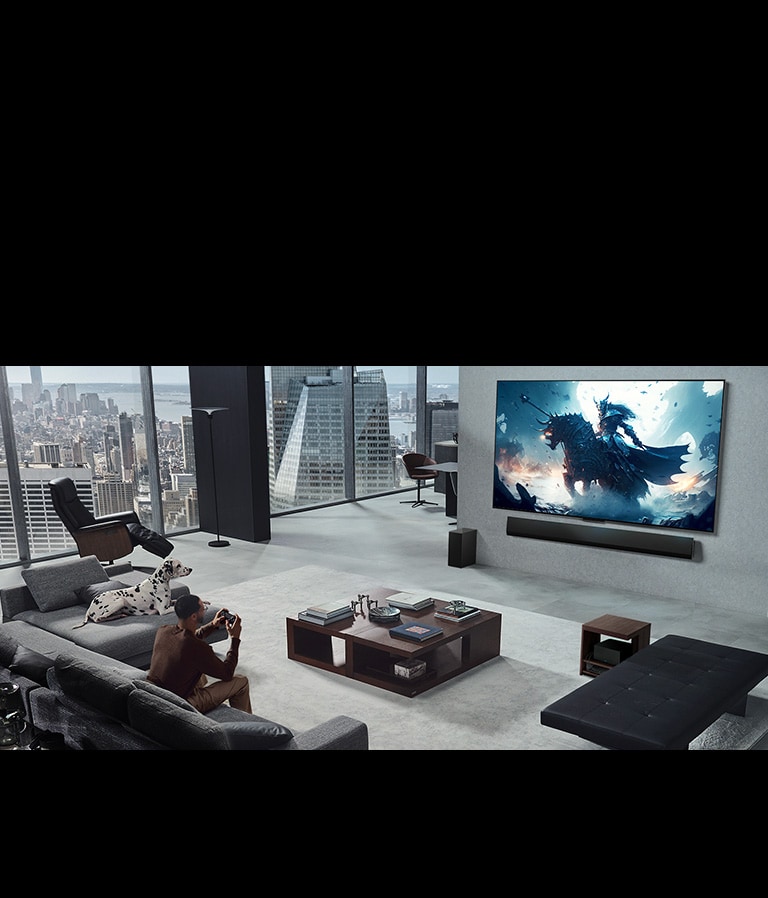 Dzīvojamā istaba ar vīrieti, spēlējot video spēli ar pie sienas piestiprinātu LG True Wireless TV un LG Soundbar. Vīrietim rokās ir kontrolieris, net spēļu konsole nav tieši redzama. Tāpat nav redzamu vadu. Zero Connect Box skaisti novietota zem sānu galdiņa un gandrīz nav saskatāma. 