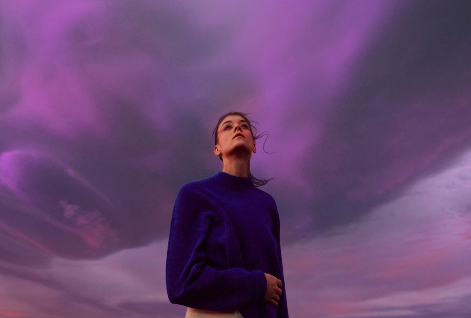 Sieviete veras uz violetām debesīm. Viņas mati viegli kustās.