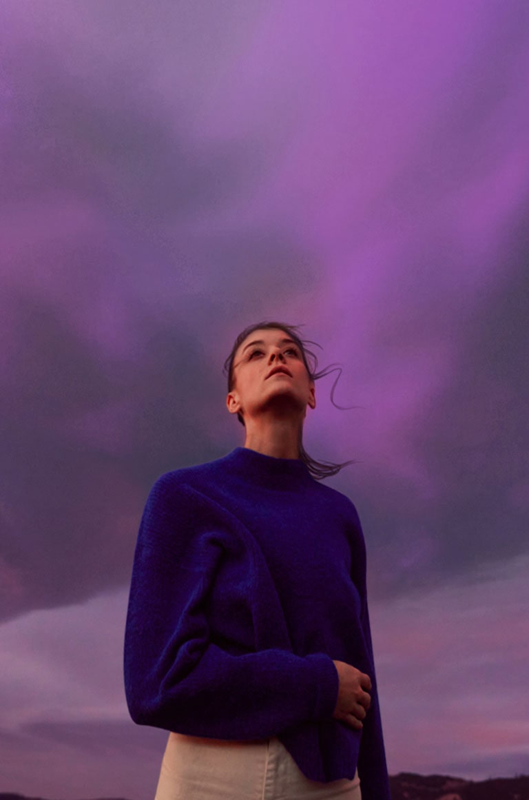 Sieviete veras uz violetām debesīm. Viņas mati viegli kustās.