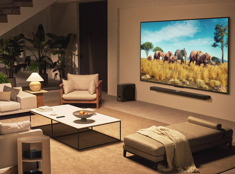 Ģimene sēž uz dīvāna ar seju pret LG QNED TV, kas piestiprināts pie sienas virs LG Soundbar, modernā dzīvojamā istabā.  Zero Connect Box atrodas kafijas galdiņā.