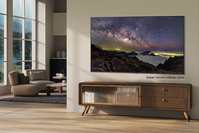 Lauku mājas interjers. Milzīgs pie sienas piestiprināts LG TV savā ekrānā rāda skaistu dabas ainavas mākslas darbu. TV izskatās kā pie sienas piekārta fotogrāfija.