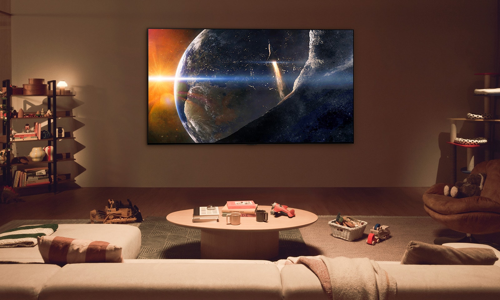 Ģimene uz grīdas samazināta apgaismojuma dzīvojamajā istabā pie neliela galdiņa, skatoties uz pie sienas piestiprinātu LG TV, kurā parādīta Zeme no kosmosa.