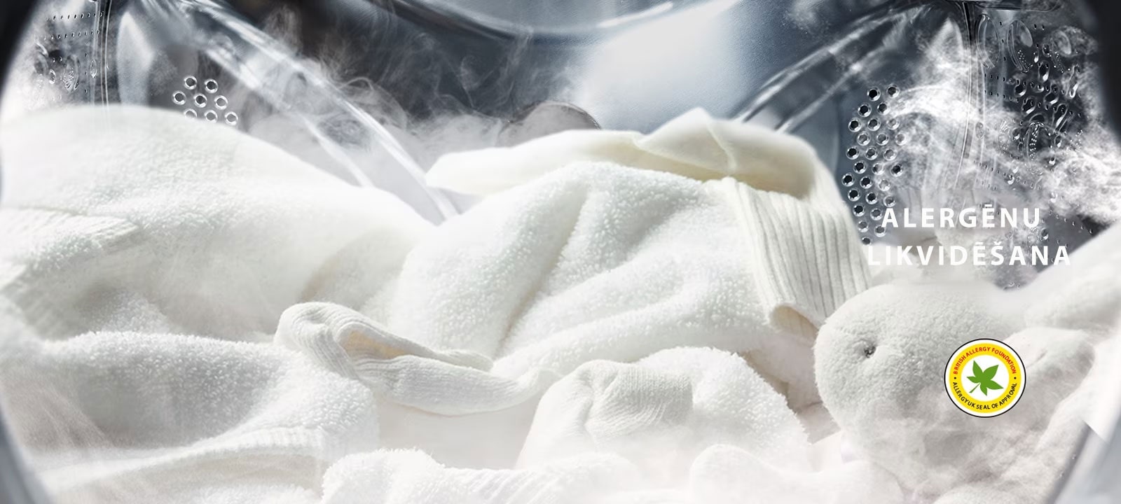 Balts halāts un mīkstā rotaļlieta redzama veļas mazgājamās mašīnas tvertnē, mazgājot ar tvaiku